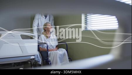 Donna seduta in abito ospedaliero di fronte alla finestra in ospedale, con sedia a rotelle e medico whitecoat Foto Stock