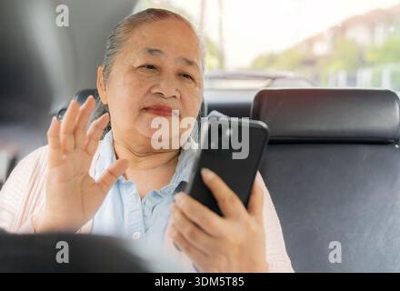 Bella donna asiatica, felice e anziana, seduta sul sedile del passeggero in auto mentre chiama i suoi amici o familiari. Foto Stock
