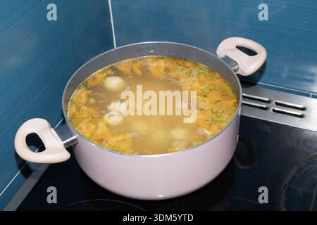Zuppa fatta in casa con gnocchi cucinati in una pentola sul piano cottura. Cucina tradizionale con brodo caldo, verdure e cibo semplice e confortevole. Foto Stock