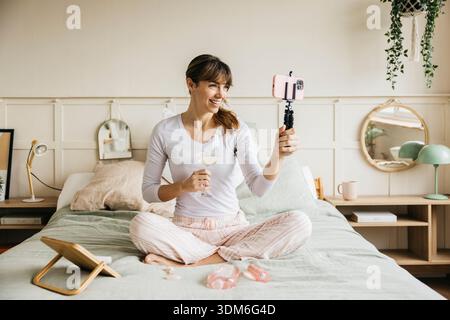 Giovane donna che crea contenuti online sulla cura della pelle e la bellezza dalla sua camera da letto Foto Stock