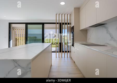 Cucina contemporanea con ripiani in marmo, pavimenti in legno e grandi porte scorrevoli all'esterno Foto Stock