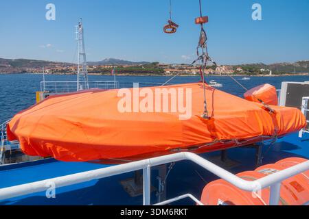 07.04.25, Olbia, Italia, battello di salvataggio arancione fissato sul ponte dei traghetti con mare sullo sfondo. Concetto di sicurezza marittima e attrezzature per navi passeggeri Foto Stock