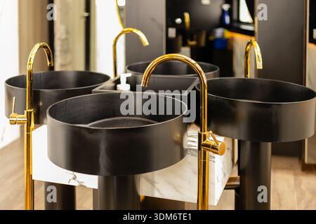 Un set di quattro lavandini rotondi neri si trova su una base in marmo in un bagno contemporaneo. I rubinetti in oro si estendono dai lavandini per un facile accesso all'acqua. Lo spazio Foto Stock