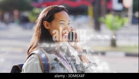 Donna parlante che tiene il telefono all'orecchio sul marciapiede della città, indossa giacca in denim e zaino con rivestimento esterno Foto Stock
