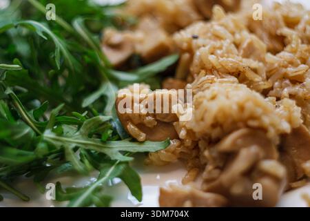 Risotto ai funghi o pilaf di riso servito con insalata di rucola verde fresca sul piatto. Cena vegetariana. Foto Stock