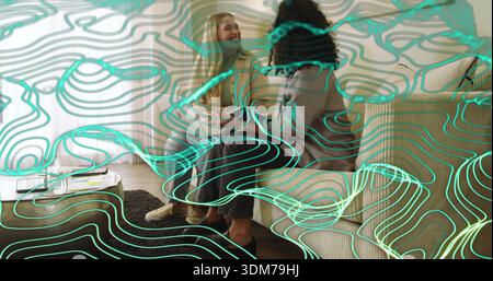 Due donne parlanti che indossano una giacca abbronzante, un maglione grigio, appoggiandosi sul divano a casa, con rivestimento turchese Foto Stock