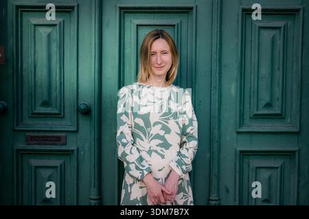 Una donna si erge davanti ad una grande porta di legno verde, indossando un abito dai motivi chiari. Guarda con calma la telecamera in luce soffusa, con un semplice Foto Stock