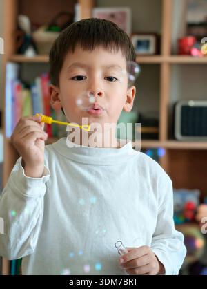 il bambino di 4 anni trasuda felicità mentre soffia bollicine a casa, catturando un momento giocoso di creatività e divertimento innocente in un ambiente accogliente e inviti Foto Stock