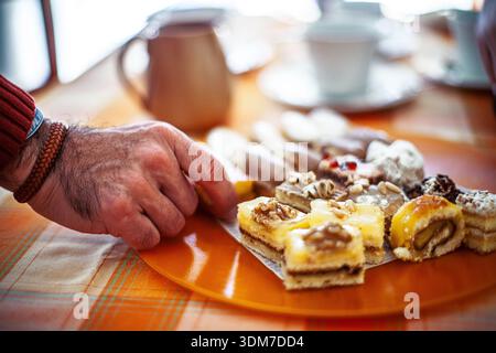 Man's Hand seleziona un dolce da un vivace piatto di dolci e dolci tradizionali assortiti a Siviglia, Spagna, con sfondo bokeh. Foto Stock