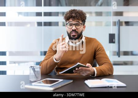 Giovane imprenditore che presenta idee aziendali e condivide informazioni importanti durante una discussione, indicando mentre tiene un notebook in una moderna scrivania Foto Stock