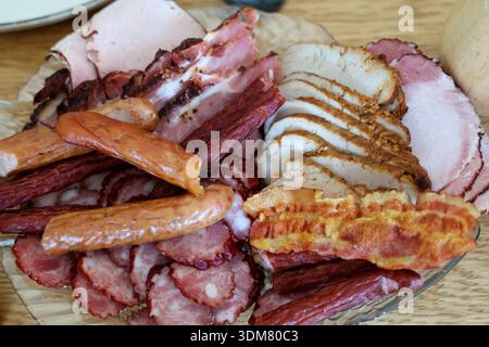 Vista dall'alto di un piatto di vetro pieno di pezzi di carne, tra cui salsicce, pancetta e prosciutto Foto Stock
