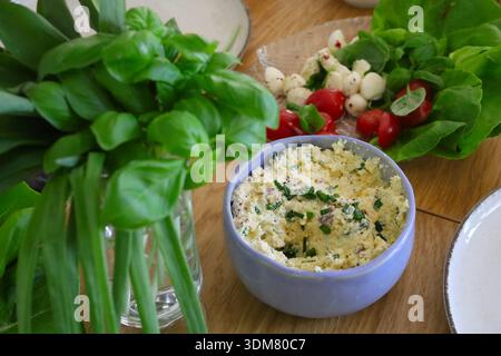 Tavola delle vacanze di Pasqua piena di cibo, tra cui pasta di uova, insalata, pomodori, mozzarella, basilico e erba cipollina Foto Stock