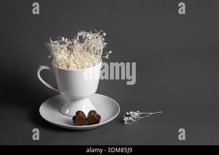 Natura morta romantica e minimalista con cioccolatini a forma di cuore e tazza bianca Foto Stock