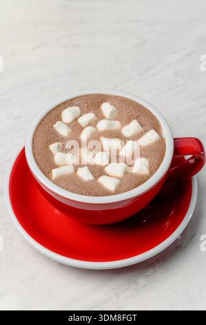 Cioccolata calda con marshmallow bianchi in una tazza di ceramica rossa. Una tazza di cioccolata calda con marshmallow bianchi per dessert in un bar interno, primo piano Foto Stock