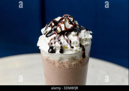Frullato di cioccolato con panna montata e ricoperto di cioccolato in un bicchiere alto. Un bicchiere di frullato di cioccolato guarnito con panna pesante e sciroppo agai Foto Stock
