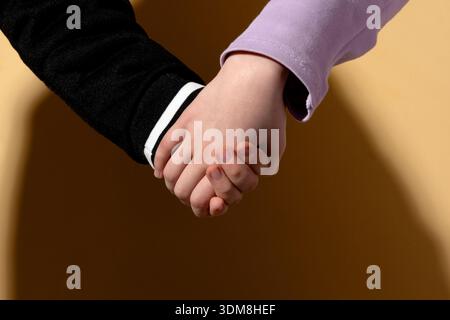 Primo piano di due bambini che si tengono per mano su un sfondo beige, simboleggiano l'amicizia, il sostegno e la solidarietà. Foto Stock