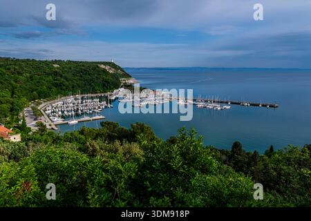 Vista ad alto angolo della Marina di Duino a Castelreggio con il Golfo di Trieste e il Faro della Vittoria in lontananza. Foto Stock