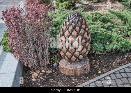 Grande cono decorativo di pino intagliato in legno come ornamento nel parco pubblico, circondato da cespugli sempreverdi e mirtillo rosso. Foto Stock