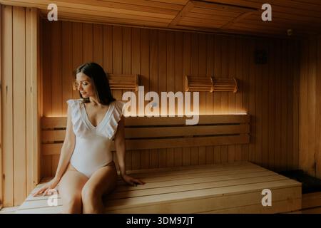 Una donna siede pacificamente in una sauna di legno, godendosi un momento di relax con un calore rilassante. Foto Stock