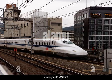 Un treno ad alta velocità della serie N700 viaggia lungo i binari ferroviari sopraelevati passando davanti a edifici urbani contemporanei. Foto Stock