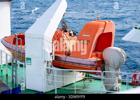 Scialuppa di salvataggio arancione fissata sul ponte della nave che rappresenta l'equipaggiamento di sicurezza e le operazioni di trasporto marittimo. Foto Stock