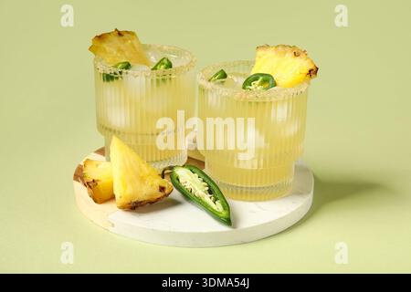 Bicchieri di gustoso cocktail di margarita con pepe jalapeno e ananas su sfondo verde Foto Stock