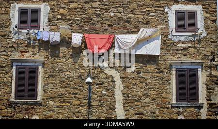 Facciata rustica in pietra con biancheria appesa e diverse finestre scure, Slovenia Foto Stock