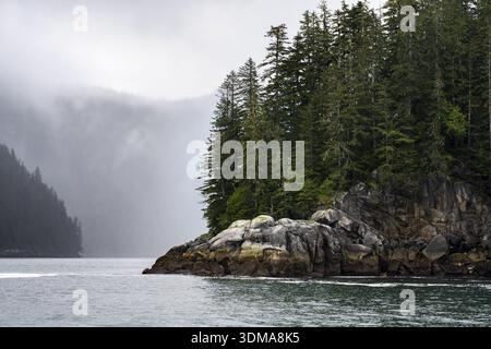 Costa rocciosa con foresta di conifere, paesaggio costiero, montagne mistiche ricoperte di nuvole, Parco Nazionale dei Fiordi di Kenai, Penisola di Kenai, Alaska, Stati Uniti Foto Stock