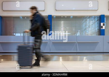 Movimento sfocato del viaggiatore che cammina con custodia nel moderno terminal dell'aeroporto Foto Stock