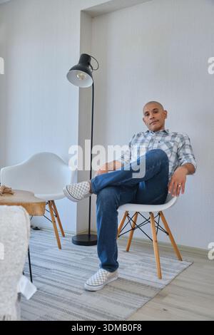 Giovane seduto su una poltrona con le gambe incrociate, guardando direttamente la telecamera Foto Stock