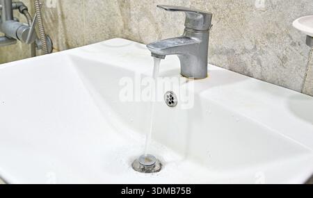 Primo piano dell'acqua che fluisce dal rubinetto del lavandino nel bagno moderno Foto Stock