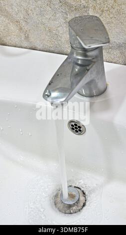Primo piano dell'acqua che fluisce dal rubinetto del lavandino nel bagno moderno Foto Stock