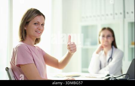 Il paziente sorridente dà un pollice su durante una consultazione positiva in un luminoso studio medico Foto Stock