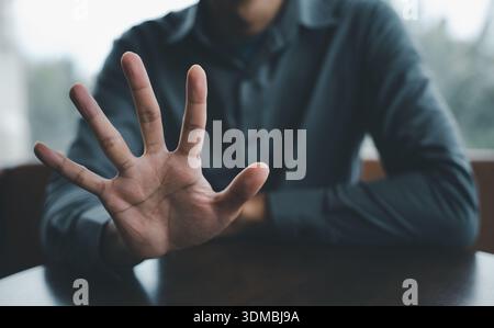 Primo piano di una mano aperta che si allontana, le dita si estendono verso la fotocamera, con uno sfondo sfocato di una persona in una camicia blu. Foto Stock