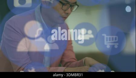 Digitare un uomo asiatico maturo con un blazer rosa e occhiali da vista alla scrivania, utilizzando un laptop con interfaccia utente traslucida Foto Stock