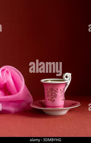 Natura morta con piccola tazza rosa e scialle rosa su sfondo marrone. Composizione minimale con atmosfera accogliente, colori tenui, elegante stile decorativo. Foto Stock