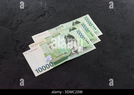 La Corea del Sud ha vinto le bollette su sfondo scuro. Vista ad alto angolo di tre banconote verdi da 10000 KRW su sfondo scuro. Foto Stock