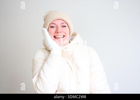 Giovane donna sorridente che indossa una giacca invernale bianca con cappuccio su uno sfondo luminoso e minimal Foto Stock
