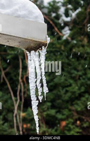 ghiaccio sospeso dal bordo del tetto innevato in inverno Foto Stock