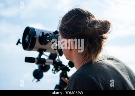 Una vista posteriore ravvicinata cattura un uomo con un telescopio professionale contro un vasto cielo blu. L'immagine mette in evidenza attrezzature astronomiche di alta qualità e l'ambiente sereno, riflettendo un profondo interesse Foto Stock