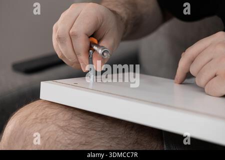 Vista ravvicinata delle mani di una persona utilizzando un cacciavite per stringere con cautela una vite per mobili in una lavagna bianca, illustrando la diligente ristrutturazione della casa Foto Stock