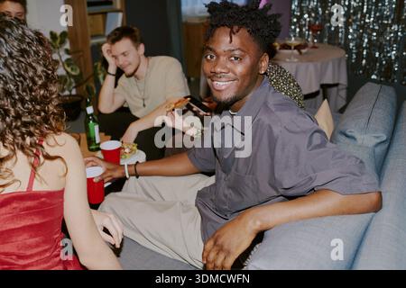 Giovane uomo Nero adulto sorridente mentre socializza con gli amici a Party Foto Stock
