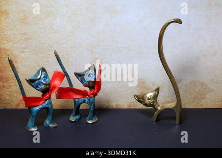 statuette in ottone vintage, due con nastri rossi coordinati e una con una forma alta e astratta, che simboleggia l'unicità e la non conformità Foto Stock
