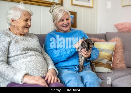 Due donne anziane con un gatto seduto su un divano a casa Foto Stock