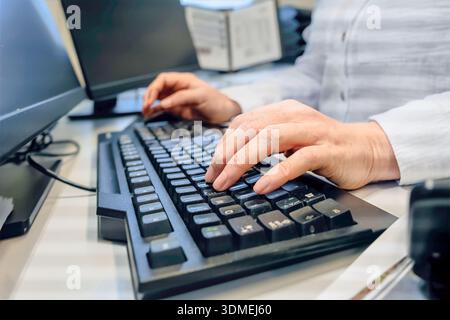 Precisione e precisione di una donna che digita le mani sulla tastiera del computer alla scrivania dell'ufficio, manica lunga bianca, area di lavoro con profondità ridotta con monitor e d Foto Stock
