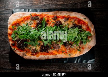 Una pizza con carne e verdure sopra. La pizza è su un tavolo nero. La pizza è molto grande e ha molti condimenti Foto Stock