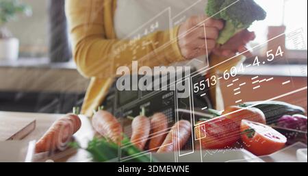 Con broccoli, una donna di mezza età che prepara le verdure al bancone della cucina, cardigan di senape e sovrapposizioni AR Foto Stock