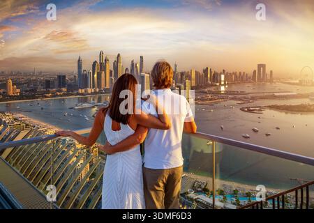 Vista posteriore di una coppia avvolgente in abiti bianchi, godendosi la splendida vista del tramonto sullo skyline di Dubai Marina, Emirati Arabi Uniti Foto Stock