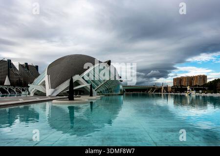 Architettura futuristica de l'Hemisfèric presso la città delle Arti e delle Scienze di Valencia, Spagna, riflessa in una piscina blu sotto un cielo nuvoloso. Foto Stock