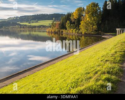 Vista dal muro della diga sul Grüntensee fino al bordo della foresta di arrampicata vicino a Nesselwang in autunno prima del tramonto. Foto Stock